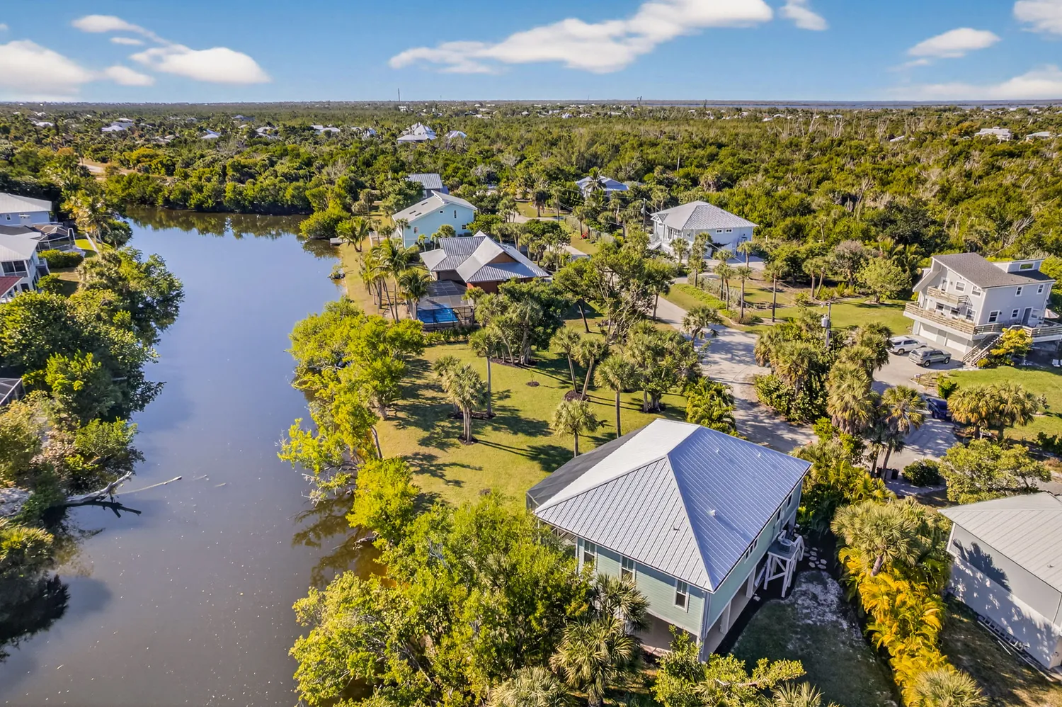 Aerial view of a waterfront neighborhood on Sanibel Island with coastal homes, palm trees, and surrounding natural landscape.